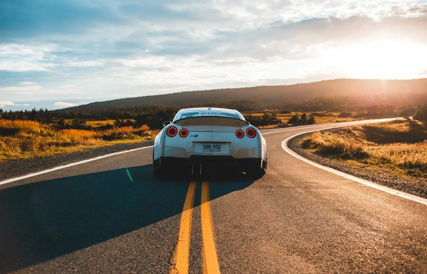 A car driving toward the sunset on a winding road.