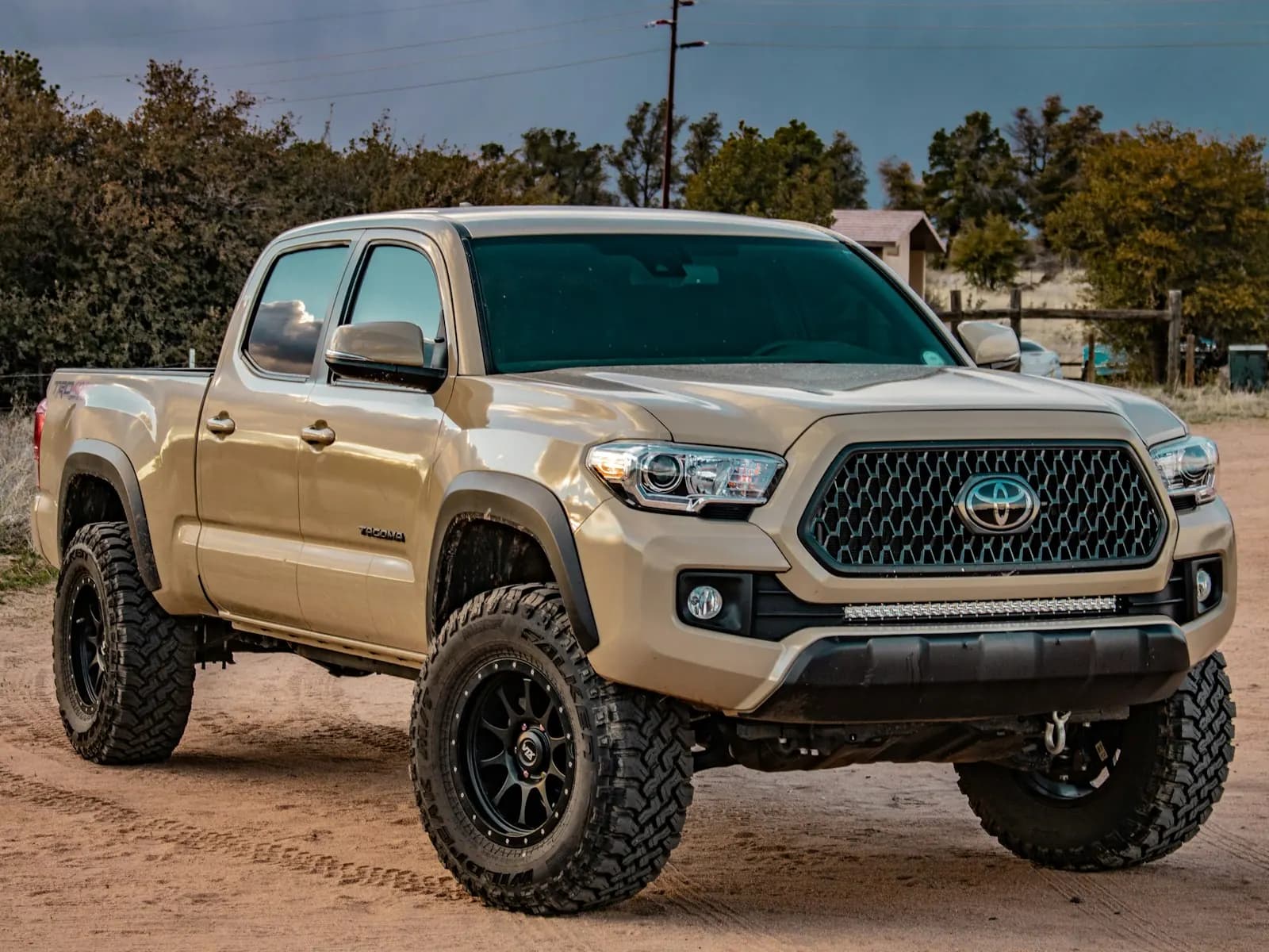 A sand-colored pickup truck parked on a dirt road